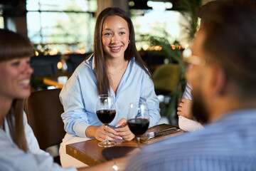 Group of cheerful business colleagues talking about something funny while drinking wine at a restaurant after work.
