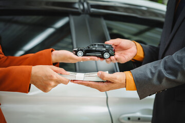 Two Asian individuals discuss a car insurance claim with an agent in front of a damaged vehicle....