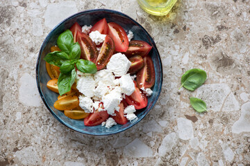 Tomato salad with ricotta and basil in a blue bowl, above view on a light-brown granite background, horizontal shot