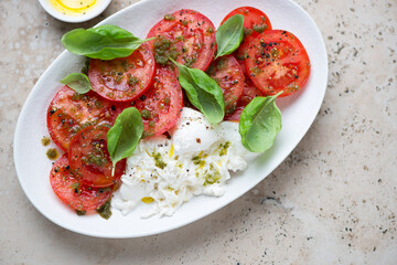 Fresh tomatoes served with basil oil and burrata, horizontal shot on a beige granite background, elevated view
