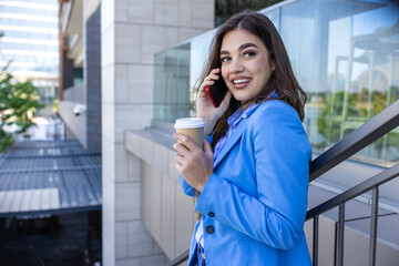 Beautiful young woman talking on her mobile phone and smiling at the staircase drinking coffee....