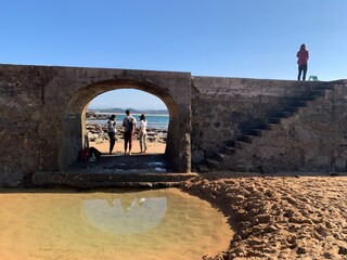 Four friends in a sand beach with a sea reflection walking on a rock construction on an adventure