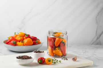 Probiotic foods. Eco friendly still life with pickled or fermented vegetables. Mini colorful bell pepper in glass jars on light grey marble background . Home food preserving or canning