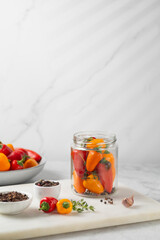 Probiotic foods. Eco friendly still life with pickled or fermented vegetables. Mini colorful bell pepper in glass jars on light grey marble background . Home food preserving or canning