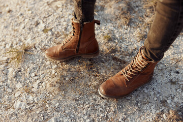 rugged adventurer standing on rural path with brown boots surrounded by grass and rocks