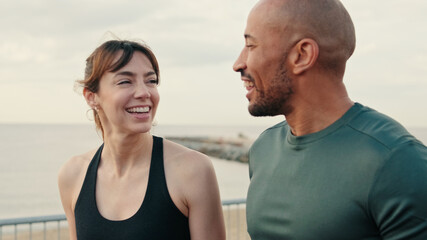 Side view of young cheerful couple in sportswear strolling along the waterfront in the morning and talking, healthy lifestyle. Couple goals and sports motivation