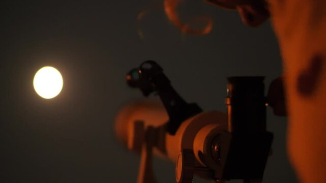 Amateur astronomer - small girl looks at the Moon through a telescope at night