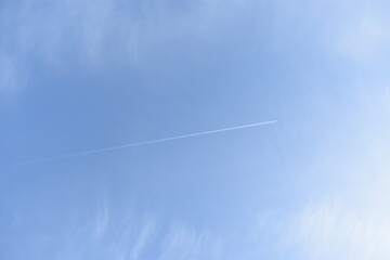 Passenger plane leaves a white trail in the sky. Сontrail of overflying passenger airplane in the clear blue sky. Plane trail in a blu sky with clouds.