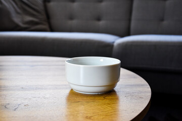 White ceramic bowl on a wooden coffee table in a cozy living room. Minimalist and modern interior design with neutral tones and comfortable furniture in the background