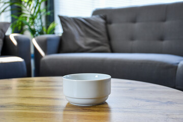 White ceramic bowl on a wooden coffee table in a cozy living room. Minimalist and modern interior design with neutral tones and comfortable furniture in the background