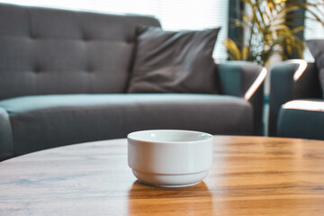 White ceramic bowl on a wooden coffee table in a cozy living room. Minimalist and modern interior design with neutral tones and comfortable furniture in the background