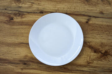 White ceramic plate on a wooden surface. Minimalist table setting, perfect for modern dining or kitchen decor with a simple and clean aesthetic