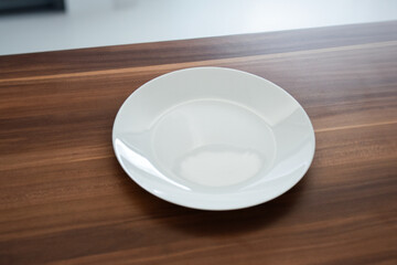 White ceramic plate on a wooden surface. Minimalist table setting, perfect for modern dining or...