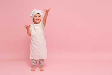 A small child in a chef's outfit poses happily in a pink-themed studio portrait, showcasing his love for cooking. Kid aged 3 years (three year old boy)