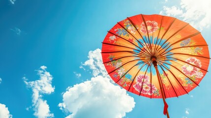 A Thai paper umbrella with a colorful floral pattern, open against a blue sky with a clear space for your message.