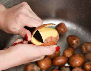 Woman peeling potatoes in a kitchen sink. Close-up. A woman peels potatoes with a knife in the kitchen, close-up. Cooking process. wash potatoes