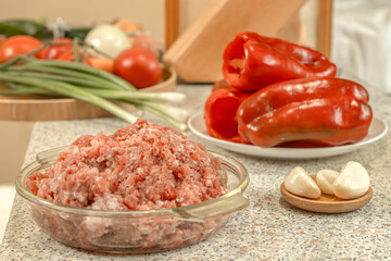 Raw minced meat against the background of peeled and prepared for stuffing red bell peppers and other vegetables.