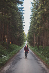 Young woman in a red plaid shirt walking down a peaceful, tree-lined forest road, embracing the tranquility and beauty of nature, symbolizing freedom and a journey of self-discovery