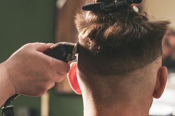 Girl hairdresser makes a haircut to a young guy using a hair clipper in a barbershop