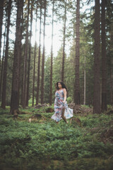 Pretty young brunette aged 20-25 is running around the forest in a colourful dress. Joy of clean air and the power of nature. Forest fairy