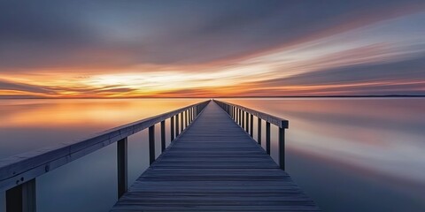 Fototapeta premium A wooden pier extends out into a calm sea at sunset, with a colorful sky and the reflection of the sun on the water.