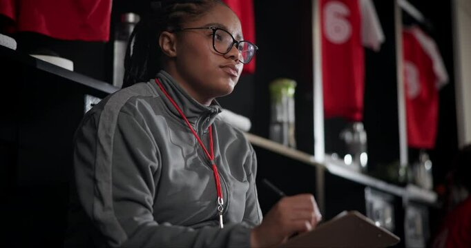 Woman, soccer coach and writing with clipboard in locker room for game plan, strategy or team formation. Young female person or football trainer taking notes for gameplay, schedule or ideas on match