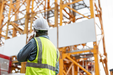 Construction site supervisor or project manager wearing a white hard hat and safety vest talking...