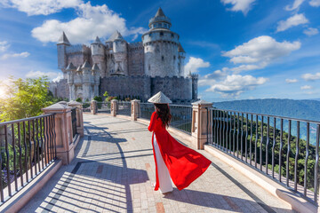 Vietnamese girl in a red ao yai dress is traveling at French village on Bana Hills in Danang,...