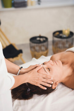 Face massage in professional salon. Therapists hands lays on the womans forehead, close-up, vertical format, selective focus.
