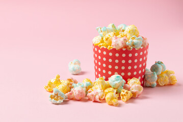 Multicolor sugary popcorn in  red papper form and scattered on a pink background with copy space
