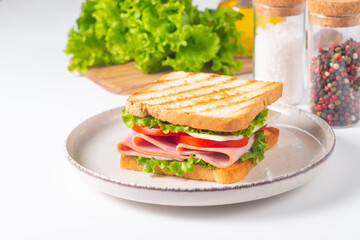 Close-up of two sandwiches with bacon, salami, prosciutto and fresh vegetables on rustic wooden cutting board. Club sandwich concept