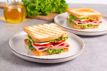 Close-up of two sandwiches with bacon, salami, prosciutto and fresh vegetables on rustic wooden cutting board. Club sandwich concept