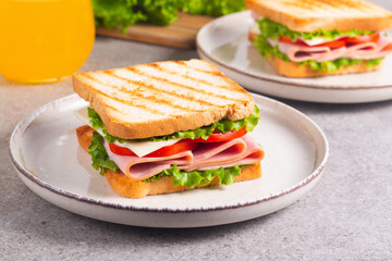 Close-up of two sandwiches with bacon, salami, prosciutto and fresh vegetables on rustic wooden cutting board. Club sandwich concept