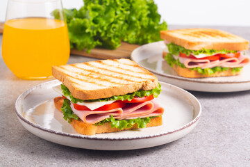 Close-up of two sandwiches with bacon, salami, prosciutto and fresh vegetables on rustic wooden cutting board. Club sandwich concept