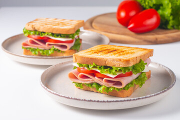 Close-up of two sandwiches with bacon, salami, prosciutto and fresh vegetables on rustic wooden cutting board. Club sandwich concept