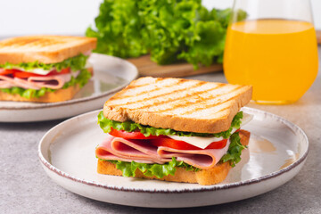 Close-up of two sandwiches with bacon, salami, prosciutto and fresh vegetables on rustic wooden cutting board. Club sandwich concept