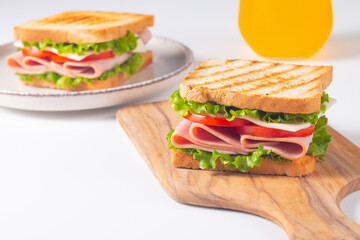 Close-up of two sandwiches with bacon, salami, prosciutto and fresh vegetables on rustic wooden cutting board. Club sandwich concept