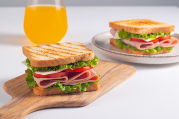 Close-up of two sandwiches with bacon, salami, prosciutto and fresh vegetables on rustic wooden cutting board. Club sandwich concept