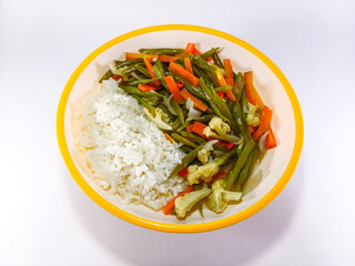 Stir-fried vegetables including green beans, carrots, cauliflower, and onions, served with rice on a plate with an orange accent, against a white background, presenting a vibrant and wholesome meal