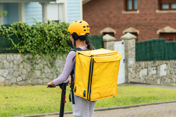 Latin food delivery girl with yellow backpack and helmet riding an electric scooter, rear view