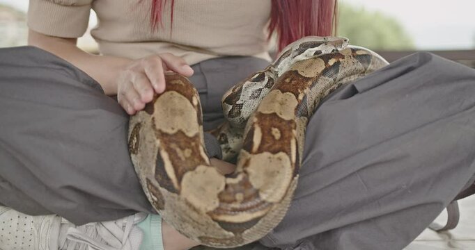 A young girl sits cross legged with her pet snake gently wrapped around her legs.