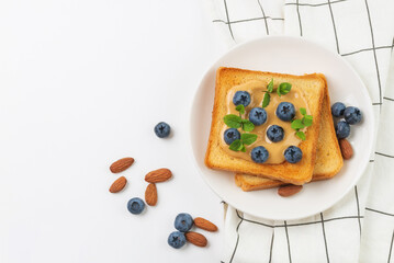 Toast with peanut butter, blueberries and fresh mint on white plate with napkin. Sandwich  for breakfast top view with copy space.