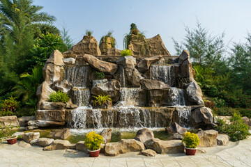 an artificial waterfall with multiple cascades, surrounded by greenery and potted plants, landscaped park or garden.