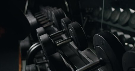 A close-up shot of a muscular male hand selecting a dumbbell from a rack in a dark, atmospheric gym. The image captures the essence of commitment and strength in fitness training. - Powered by Adobe