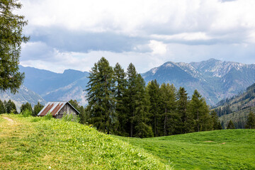 A rustic cabin nestled in the lush green valley surrounded by mountains on a cloudy day in the serene countryside