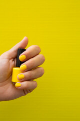 Woman's hand with yellow nails holding a bottle of nail polish.