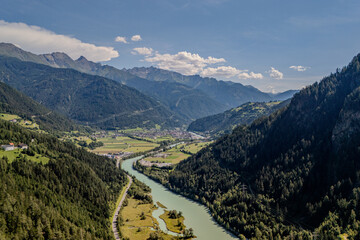 Aerial view of a winding river amidst lush green valleys and mountains during a clear day in the Swiss Alps