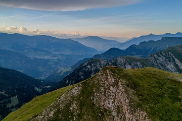Aerial view of a mountain ridge at sunset with lush green slopes and distant peaks in the distance