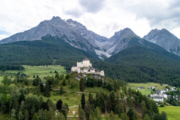 Aerial view of a historic castle nestled in green valleys surrounded by majestic mountains in the Alps during daylight