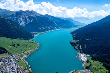Aerial view of a turquoise lake surrounded by mountains and lush green landscapes on a sunny day